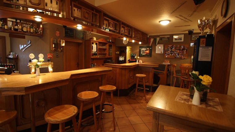Un bar confortable avec un comptoir en bois et des tabourets. Des images sont accrochées aux murs et il y a une atmosphère accueillante.