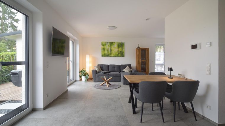 Een moderne woonkamer met een gezellige bank en een eettafel. Grote ramen zorgen voor veel daglicht en een ontspannen sfeer.