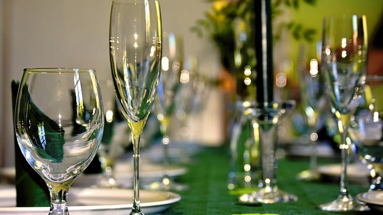 Ein festlich gedeckter Tisch mit Gläsern und einer schwarzen Kerze. Der Tisch ist mit einem grünen Tuch und frischen Blumen dekoriert.