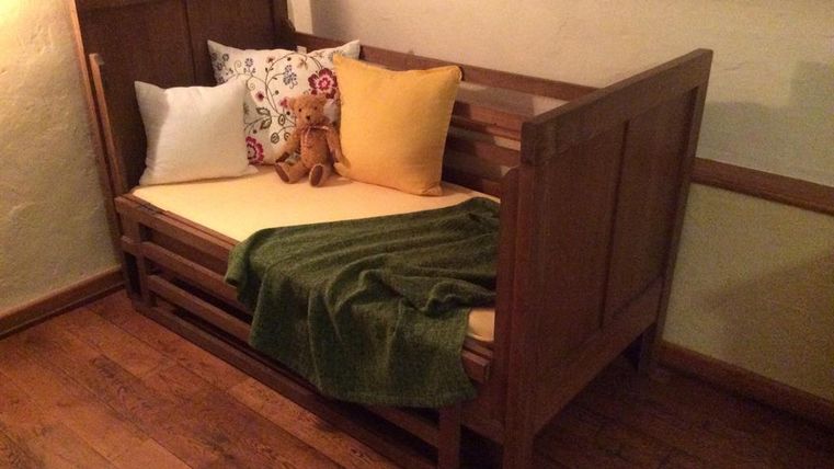 Une chambre confortable et lumineuse avec un lit en bois. Le lit est décoré de coussins colorés et d'une couverture verte.