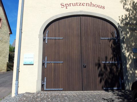 Een grote, gesloten houten deur met metalen beslag. Boven staat het woord "Sprutzenhaus".