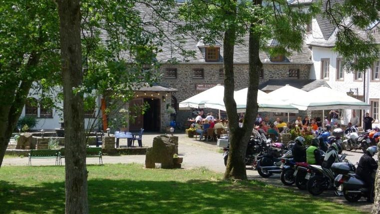 A cozy tavern with shady trees and a terrace. Many people are sitting outside and enjoying the atmosphere.