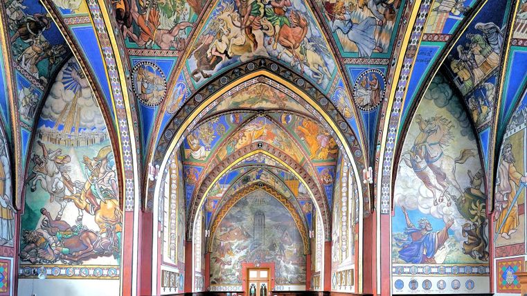 Eine prächtige Kirche mit bunten Wandmalereien und hohen, gewölbten Decken. Der Raum strahlt eine majestätische und historische Atmosphäre aus.