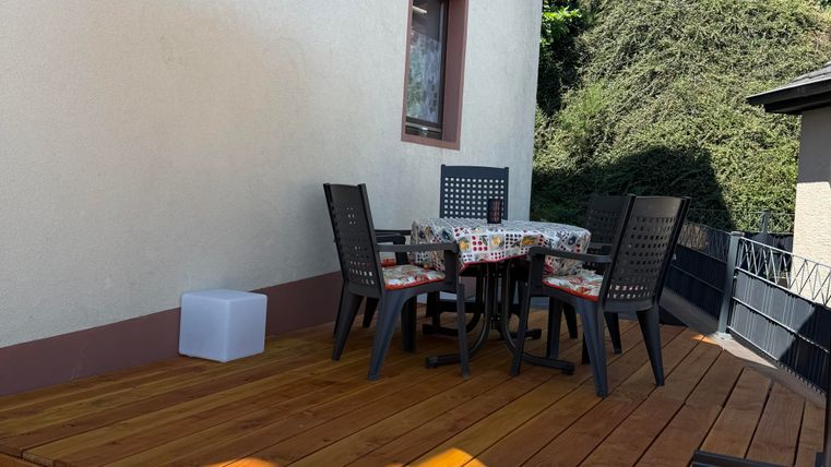 Eine gemütliche Terrasse mit einem Holzdeck und einem großen Sonnenschirm. Ein runder Tisch mit Stühlen lädt zum Verweilen ein.