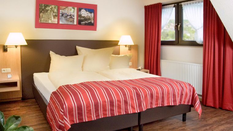 Une chambre confortable avec un grand lit et des rideaux rouges. Un éclairage doux crée une atmosphère accueillante.