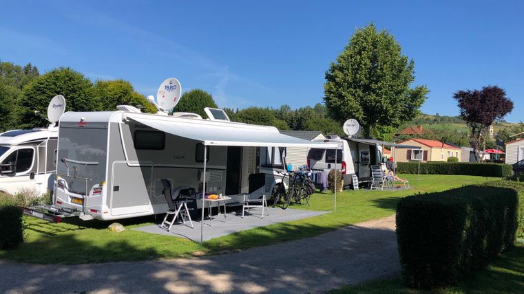 Ein Campingplatz mit mehreren Wohnmobilen und einem klaren blauen Himmel. Umgeben von grüner Landschaft und Bäumen.