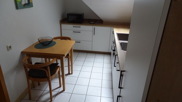 Une petite cuisine moderne avec une table et des chaises. Les murs sont clairs, et il y a un micro-ondes ainsi que des meubles de cuisine.