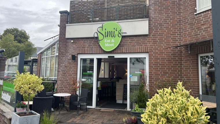 A cozy restaurant named "Simi's Eat & Meet". The entrance is surrounded by plants and seating areas.