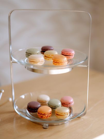 Ein elegantes Dessert-Display mit verschiedenen Macarons in bunten Farben. Die Macarons sind auf zwei transparenten Ebenen angeordnet.