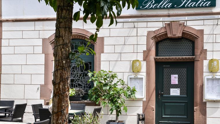A pizzeria named "Bella Italia" with an inviting outdoor terrace. The entrance is green, and there is a plant nearby.
