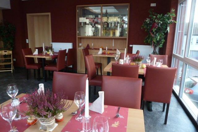 Een gezellig restaurant met houten en rode accenten. De tafels zijn mooi gedecoreerd en er zijn grote ramen die veel licht binnenlaten.