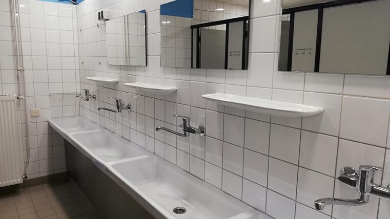 Een schoon badkamer met meerdere wastafels en spiegels. De muren zijn betegeld en de verlichting is helder.