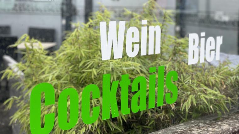 A window with labels for drinks. The words "Wine", "Beer", and "Cocktails" are clearly visible, surrounded by plants.