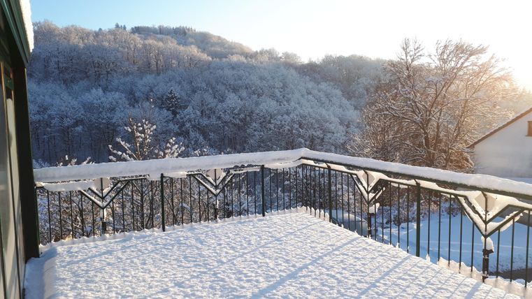 A snowy terrace with a view of a winter forest. The sun is shining, bathing the scene in warm light.