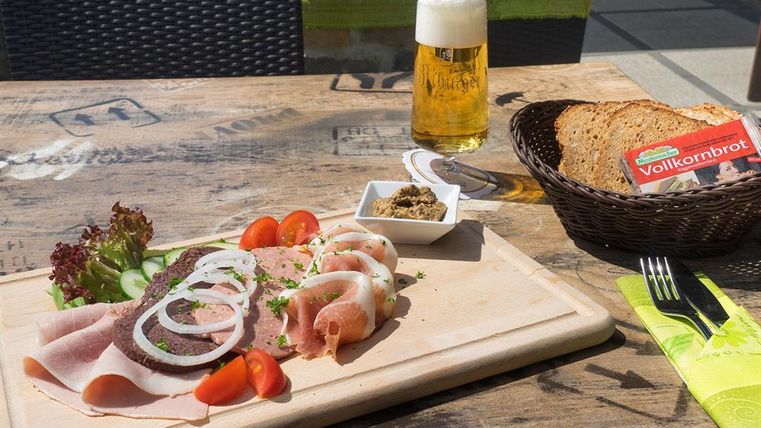 Ein köstliches Brett mit Aufschnitt, buntem Gemüse und Brotscheiben. Daneben steht ein Glas Bier auf einem Holztisch.