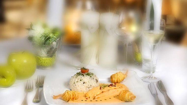 Een elegant gerecht met zalm, rijst en een kleine tomaat op een wit bord. Op de achtergrond zijn glazen en groene appels te zien.