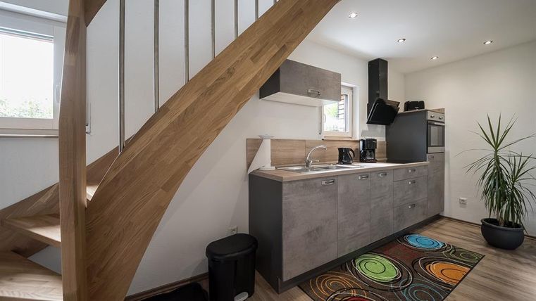 Une cuisine moderne avec un escalier en bois et un tapis coloré.
Des murs clairs et une plante créent une atmosphère conviviale.