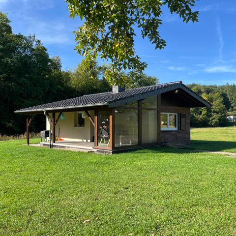 Ein modernes Haus inmitten einer grünen Wiese. Der Himmel ist klar und die Umgebung ist von Bäumen umgeben.