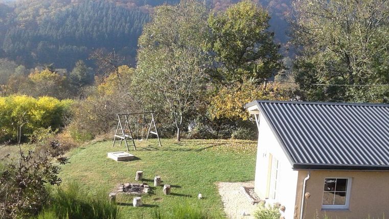 Une maison confortable entourée d'arbres et d'une pelouse verte. À l'arrière-plan, on voit des collines douces et des feuilles d'automne colorées.