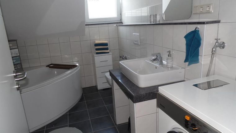 Een moderne badkamer met een badkuip en een wasmachine. Er is een wastafel en lichte tegels die de ruimte schoon en uitnodigend laten lijken.