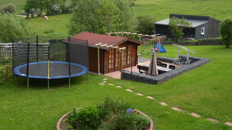 Een ruime tuin met een trampoline, een speelplaats en een klein tuinhuisje. Het groene gazon nodigt uit tot spelen en ontspannen.