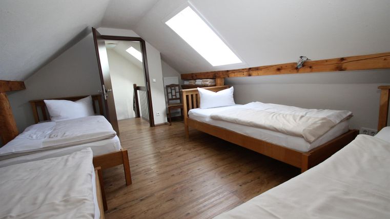 Ein gemütliches Zimmer mit drei Einzelbetten und einem Holzfußboden. Das Licht fällt durch ein Dachfenster und schafft eine helle, einladende Atmosphäre.