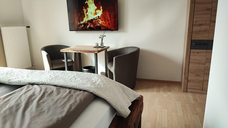 Ein gemütliches Schlafzimmer mit einem großen Bett und einem Fernseher, der ein Feuer zeigt. In der Ecke stehen ein Tisch und zwei bequeme Stühle.