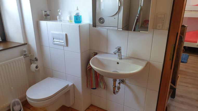 Une salle de bains moderne avec des toilettes et un lavabo. Les murs sont carrelés en clair et il y a un miroir ainsi qu'une machine à laver à l'arrière-plan.