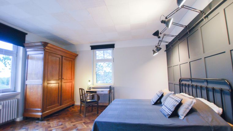 Ein einfaches Schlafzimmer mit einem großen Bett und einer Holzkommode. Die Wände sind dunkel, und es gibt ein Fenster mit Blick nach draußen.