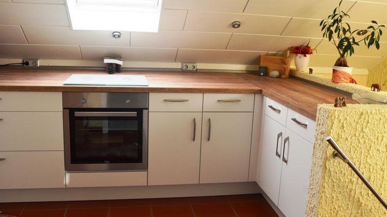 A cozy loft kitchen with white cabinets and a wooden countertop. A large skylight lets in plenty of daylight.