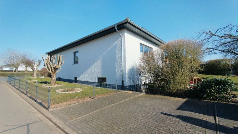 Ein modernes, weißes Haus mit einem gepflegten Garten. Die Umgebung ist ruhig und freundlich.