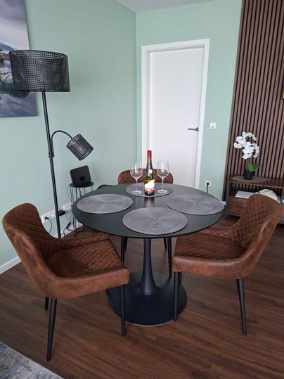 A modern dining area with a round black table and four chairs. On the table stands a bottle of wine and glasses, surrounded by stylish lighting.