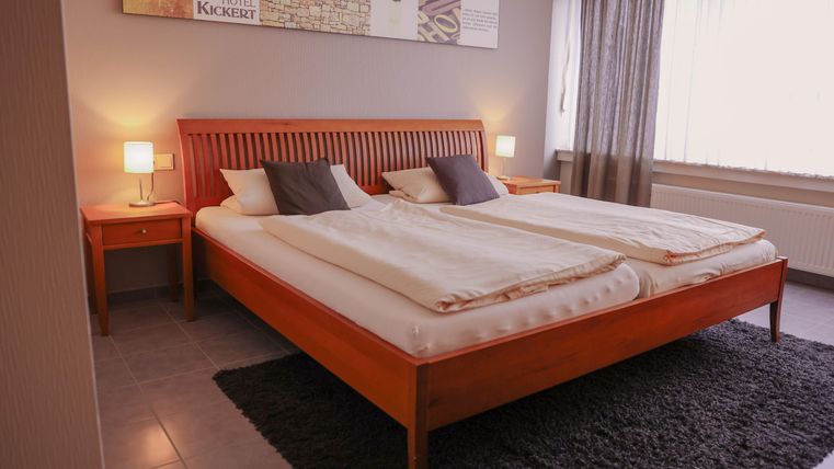 Une chambre confortable avec un grand lit double et deux tables de nuit. La pièce est lumineuse et accueillante, avec un tapis moderne et des rideaux.