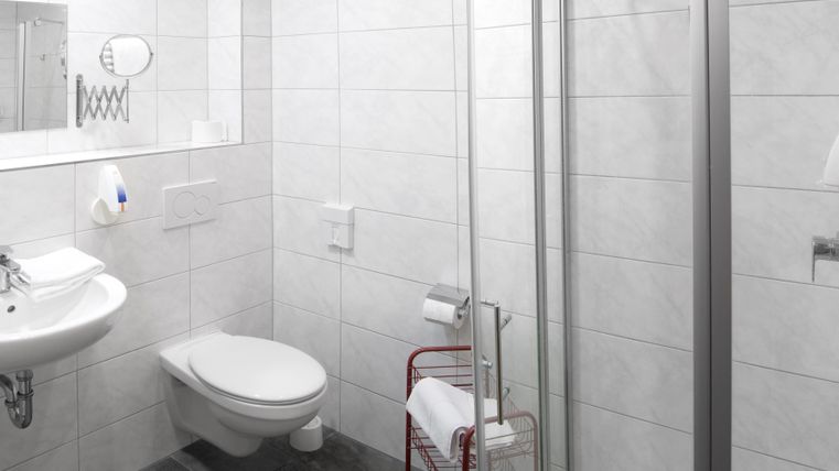Une salle de bain moderne avec des carrelages blancs et une cabine de douche transparente. Il y a un lavabo, une cuvette de toilettes et un porte-serviettes.