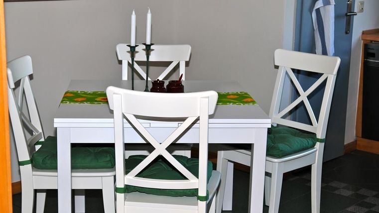 Ein heller Essbereich mit einem weißen Tisch und vier Stühlen. Auf dem Tisch liegen eine grüne Tischdecke und Kerzenhalter.