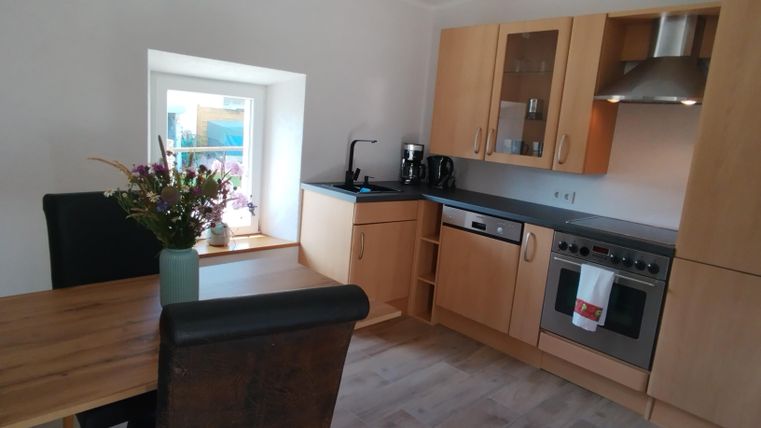 Een moderne keuken met lichte houten meubels en een grote vensterbank. Op de tafel staat een vaas met verse bloemen, en de keukenapparaten zijn goed zichtbaar.