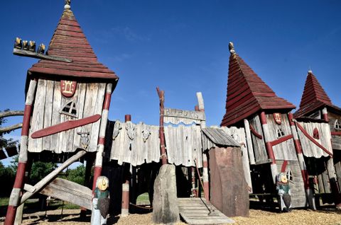 Un terrain de jeu avec des châteaux en bois et des toits rouges. Le ciel est bleu et les environs sont ensoleillés.