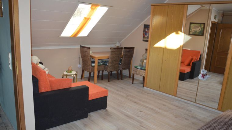 A cozy attic apartment with an orange sofa and a dining table. The room is bright and well-furnished, with a large mirror and skylights.