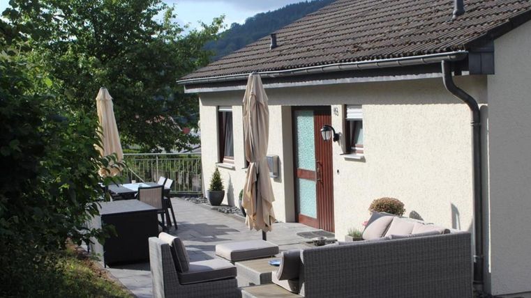Ein modernes Haus mit einer Terrasse und gemütlichen Möbeln. Die Umgebung ist grün und einladend, ideal zum Entspannen im Freien.