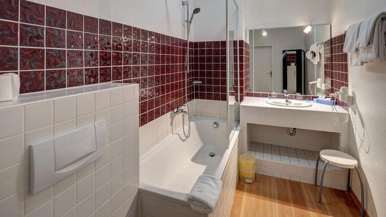 Une salle de bain moderne avec une baignoire et des carreaux blancs. Les murs sont partiellement revêtus de carreaux rouges, et il y a un grand miroir au-dessus du lavabo.