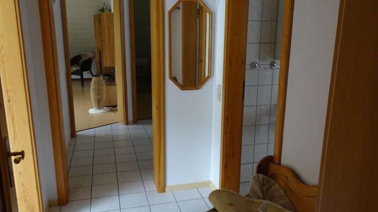 Un couloir lumineux avec des portes en bois et un miroir. À l'arrière-plan, d'autres pièces et meubles sont visibles.