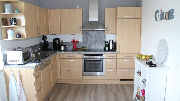 Eine moderne Küche mit Holzschränken und grauen Wänden. Die Ausstattung umfasst eine Mikrowelle, einen Herd und frisches Obst auf der Arbeitsplatte.