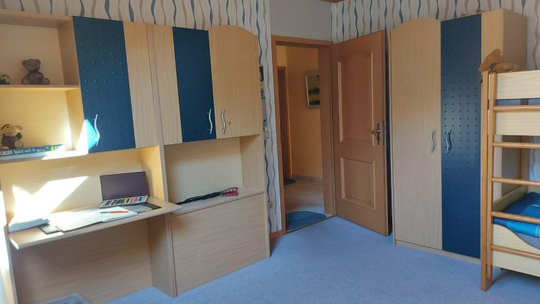 Een lichte, kindvriendelijke kamer met een stapelbed en een bureau. De muren zijn versierd met een blauw en wit patroon.