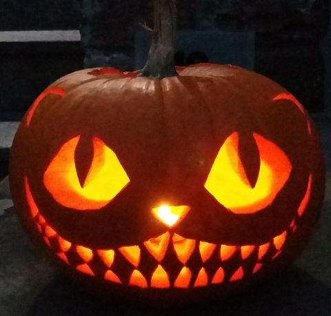 Ein leuchtender Halloween-Kürbis mit einem grinsenden Gesicht und spitzen Zähnen. Die Augen sind groß und ausdrucksvoll, was eine gruselige Atmosphäre schafft.