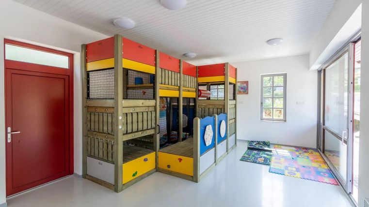 Een lichte speelruimte met kleurrijke speelstructuren en een gemakkelijk toegankelijke ingang. De ruimte is goed verlicht en kindvriendelijk ingericht.