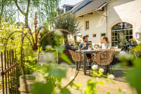 Een gezellige tuin met een tafel waar een stel zit en geniet van drankjes. Op de achtergrond is een licht huis en groene planten te zien.