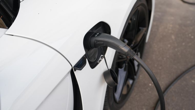 Ein weißes Elektroauto, das an einer Ladestation aufgeladen wird. Der Ladestecker ist in die Fahrzeugöffnung eingesteckt.