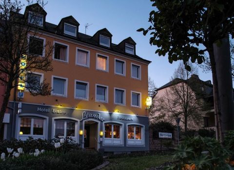 Un hôtel confortable avec un bistro et un restaurant accueillants. La façade est peinte en orange et éclairée au crépuscule.