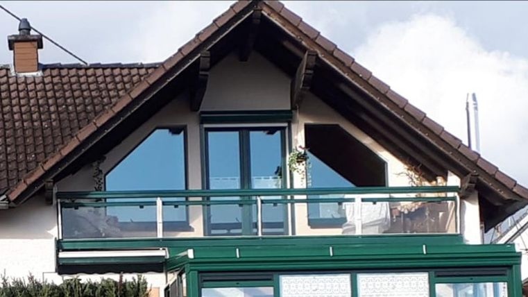 A modern house with a balcony and large windows. The sky is partly cloudy.