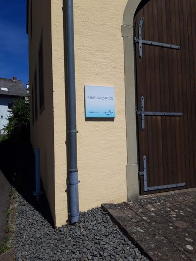 Een E-bike oplaadpunt aan een muur. Het station is goed zichtbaar en vriendelijk vormgegeven.